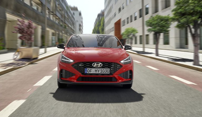 A red car driving down a street
Description automatically generated